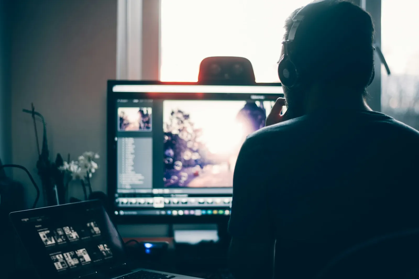 Silueta de una persona editando contenido frente a dos pantallas, con luz natural de ventana