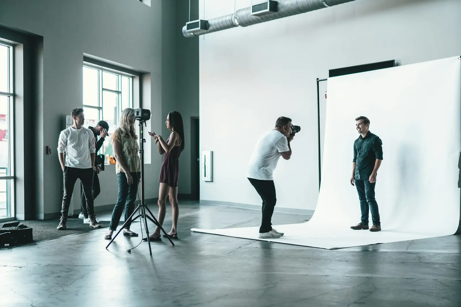 Fotógrafo retratando a una persona contra un fondo blanco, con el equipo mirando en un estudio luminoso